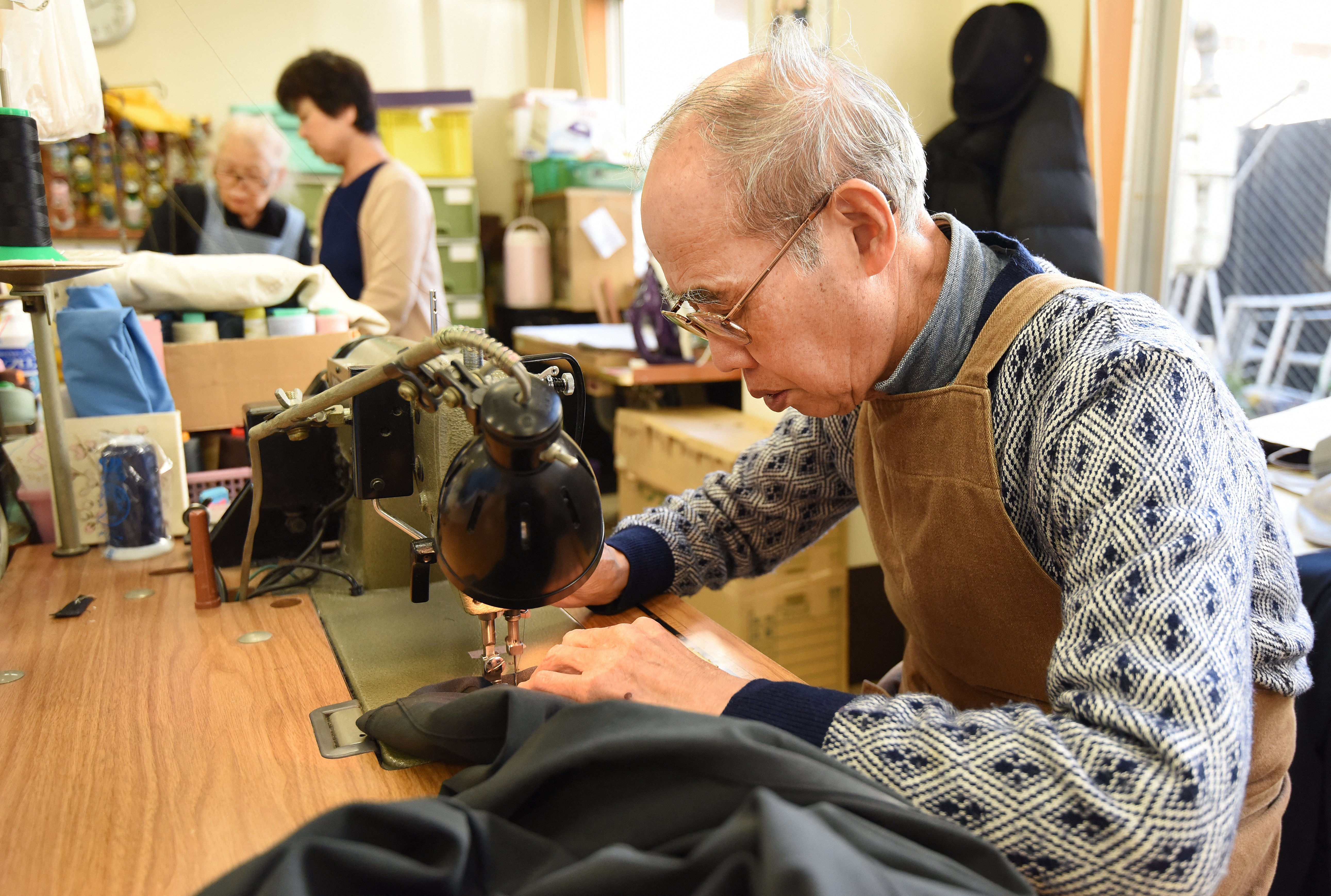 高齡社會出現延後退休的趨勢。圖為2015年12月18日，日本東京一處高齡者就業中心的工人正在修補衣物。（攝影／TORU YAMANAKA／AFP）