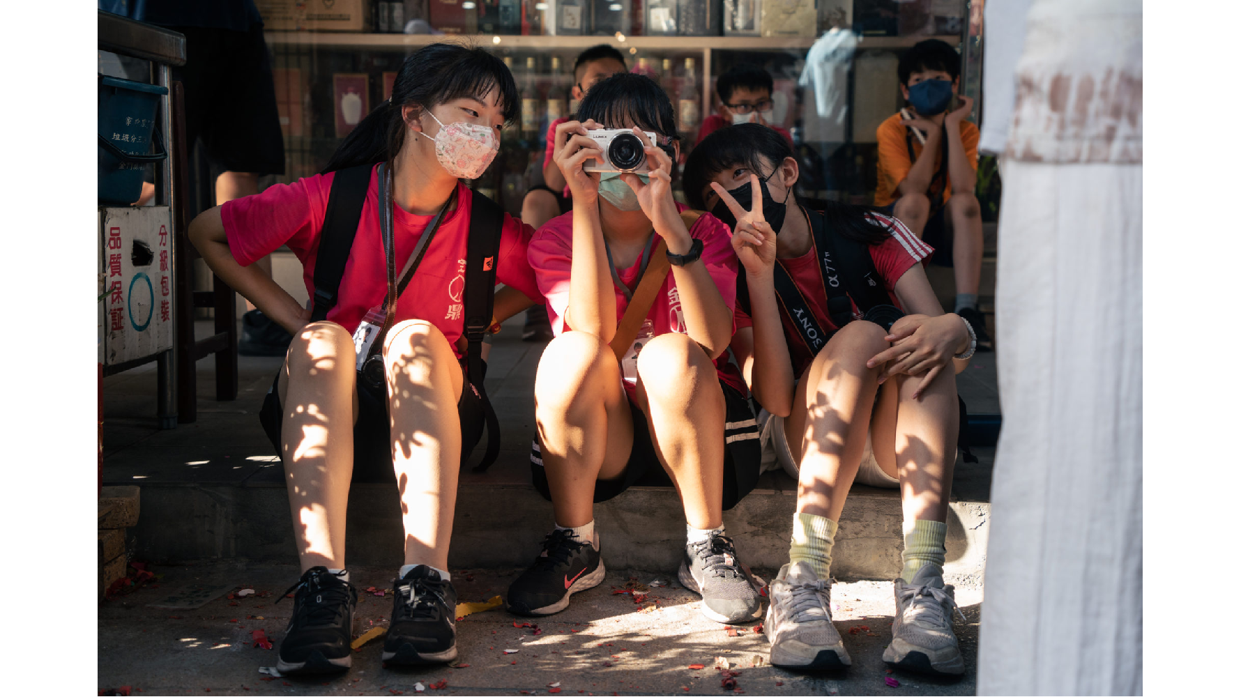 遶境空擋，金鼎國小的小記者坐在街道兩側的騎樓休息，互相查看彼此拍到的照片。